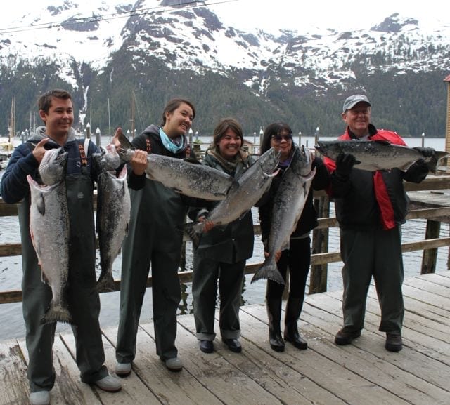 A group of people holding fish on top of a dock.