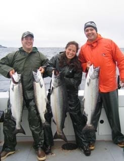 Three people holding up fish on a boat.