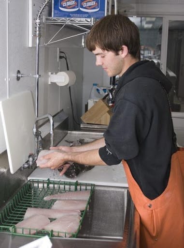 A man in an orange apron is washing fish.